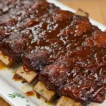 A plate of tender beef back ribs glazed with a tangy marinade, served with fresh herbs and a side of vegetables.