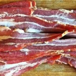 Slices of perfectly smoked beef bacon arranged on a wooden board.