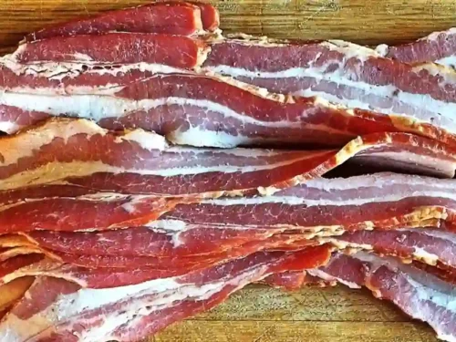 Slices of perfectly smoked beef bacon arranged on a wooden board.