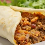 A cheesy Beefy Melt Burrito filled with seasoned beef, Spanish rice, Fritos, and homemade nacho cheese sauce.
